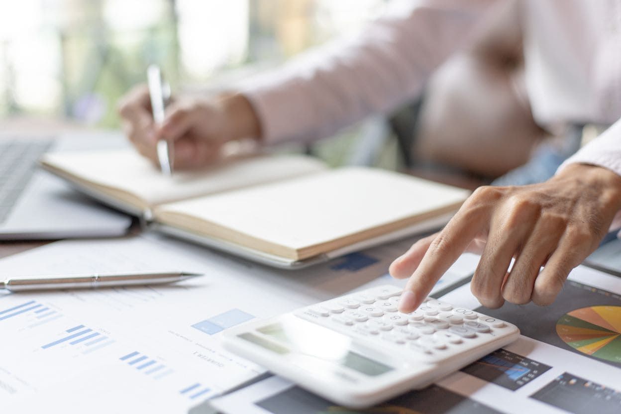 Persona usando una calculadora y revisando notas financieras para planificar gastos y presupuesto personal.